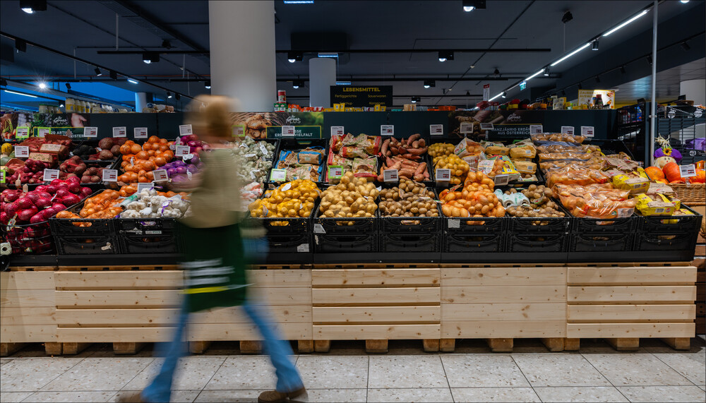 Saisonales Obst und Gemüse im Supermarkt: Frau geht schnell vorbei an Regalen voller Gemüse. | © Land schafft Leben