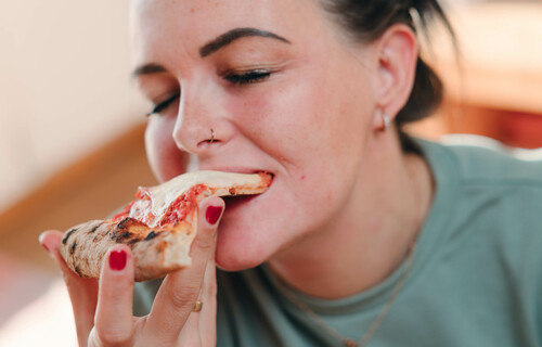 Frau beißt genüsslich in Pizzastück | © Land schafft Leben