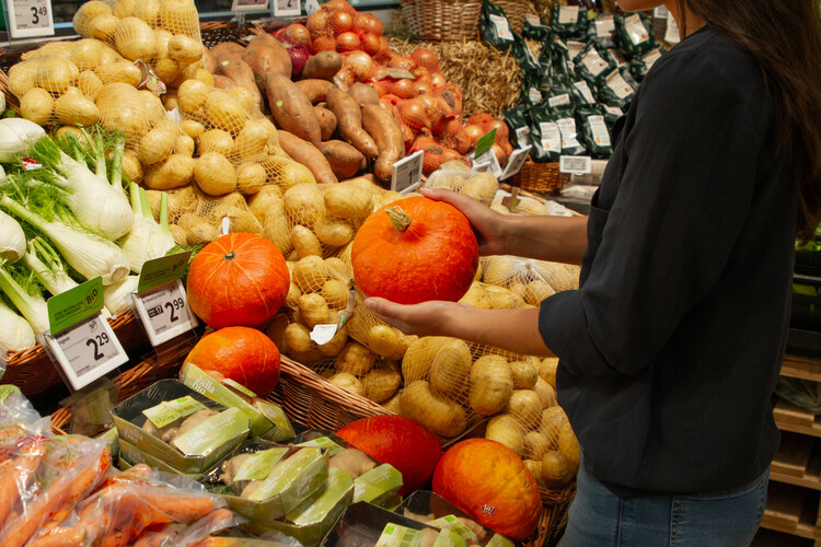 Dunkelhaarige Frau hält Kürbis im Supermarkt | © Land schafft Leben