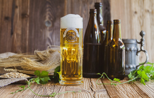 Volle Bierglas auf Holztisch mit braunen Bierflaschen im Hintergrund | © Land schafft Leben