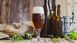 Volles Bierglas auf Holztisch vor dunklen Bierflaschen | © Land schafft Leben