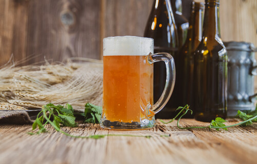 Mit orangefarbenem Bier gefülltes Henkelglas auf Holztisch | © Land schafft Leben