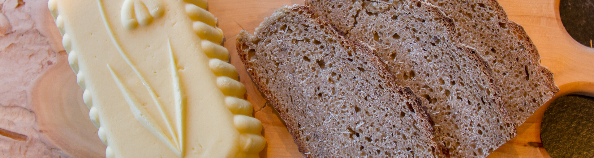 Verziertes Stück Butter liegt neben Schwarzbrot auf Holzbrett | © Land schafft Leben