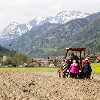 Traktor vor zwei Personen auf Feld | © Land schafft Leben